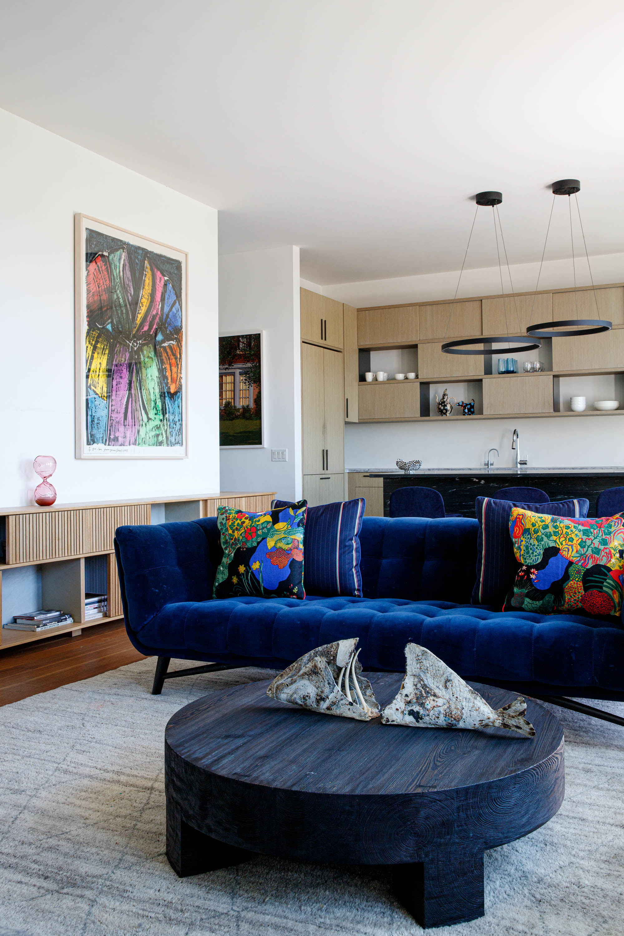 Layered living room interior with custom kitchen, blue sofa, and art in Greenpoint Brooklyn apartment by Natasa Tuohy Studio